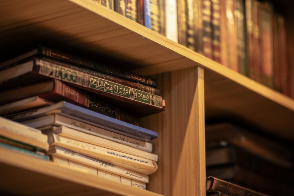 pexels-photo-31679271 A stack of Islamic religious books on a wooden shelf, highlighting Arabic scripts and cultural significance.